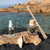 Un spray senteur Corse dans un flacon transparent, une pierre à parfumer avec sa ficelle et un diffuseur Corse avec ses anches, poser sur un morceau de bois à flotter et sur une nappe noir. La mer et les rochers composent l'arriere plan 