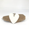 Pierre à parfumer en céramique artisanale Corse couleur blanche en forme de coeur avec une ficelle, posé sur du bois à flotter.